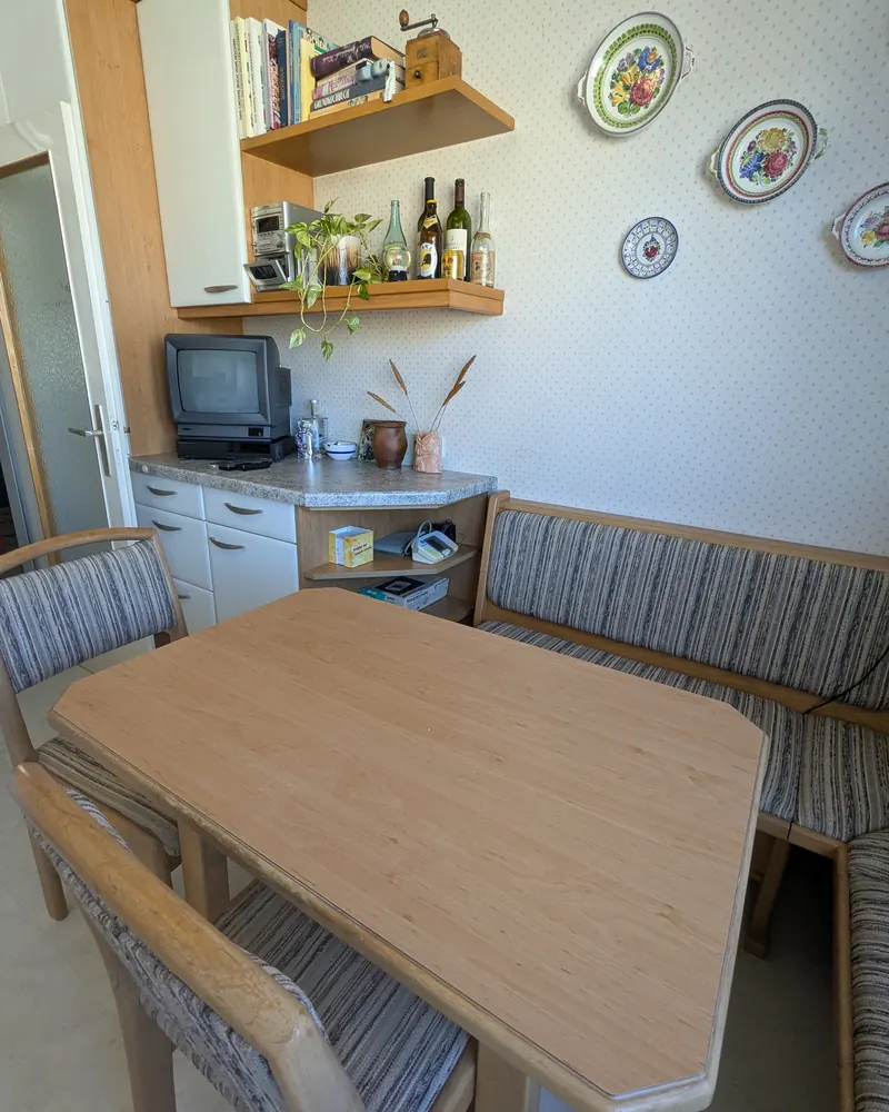 Eckbank nachher: freie Bank und leerer Holztisch, Regal mit Büchern und Tellern an der Wand.